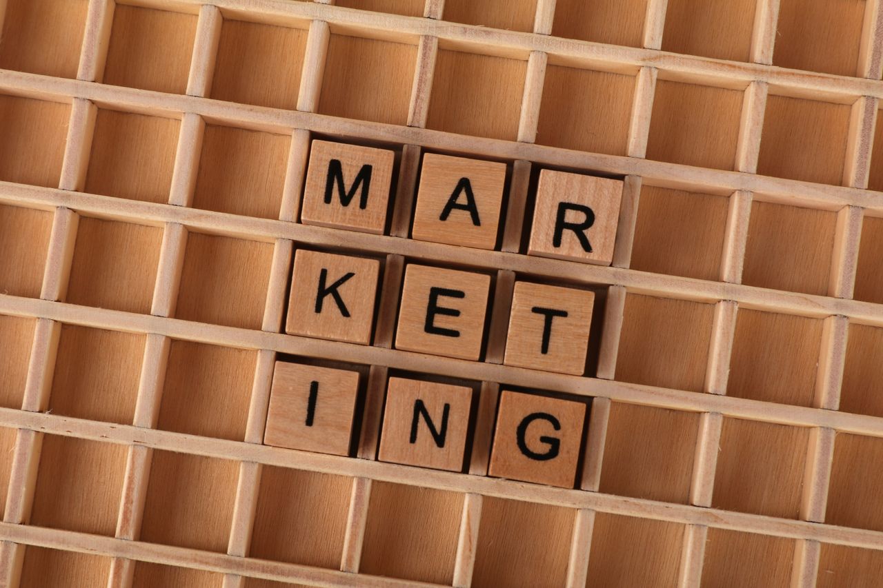 heros-img Wooden letter tiles spell out the word marketing on a grid background, showcasing creativity and business concept.